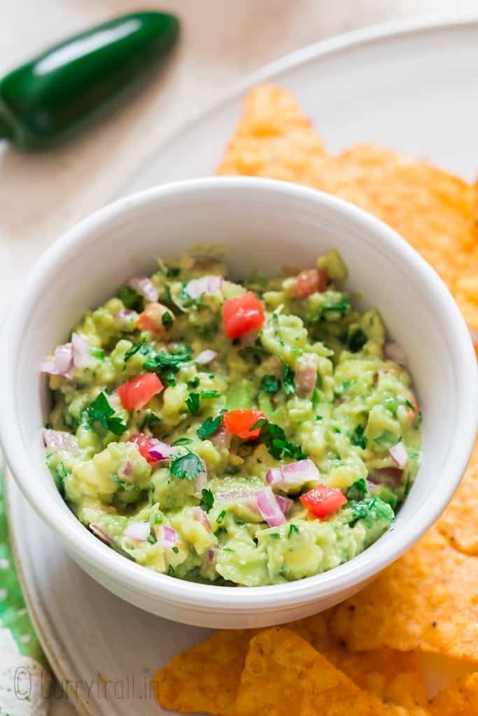 guacamole served in white bowl with nachos on sides