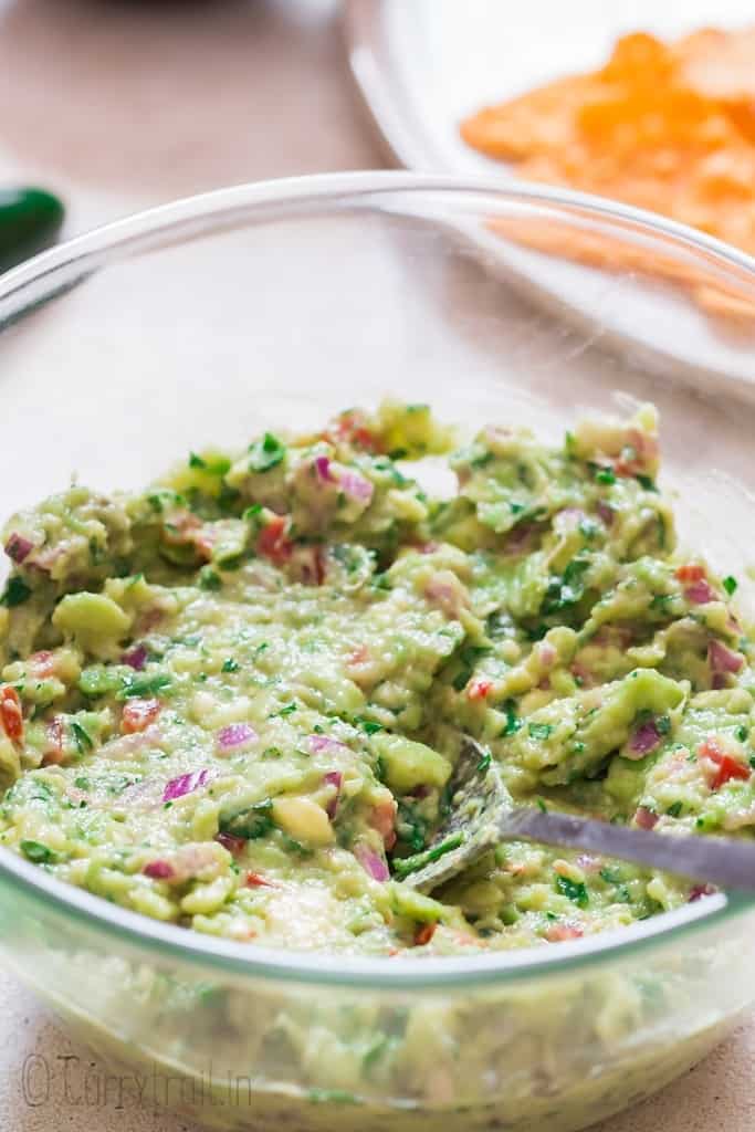 guacamole mixed in glass bowl with spoon