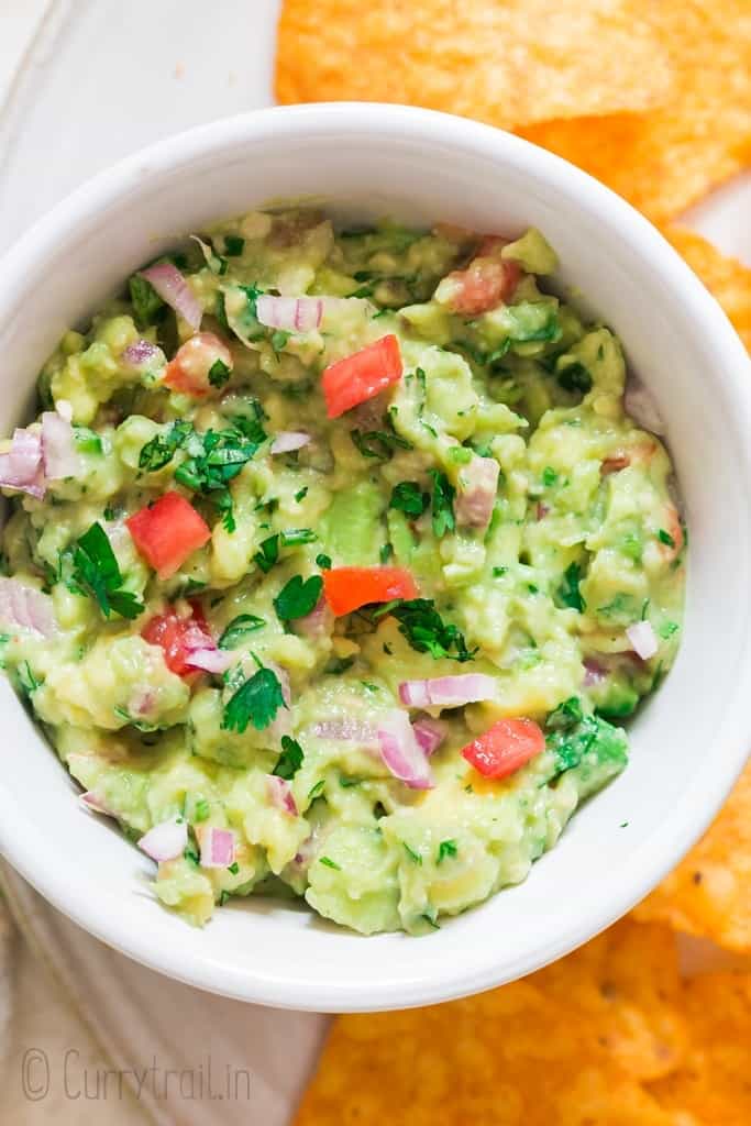 guacamole served in white bowl with nachos on sides