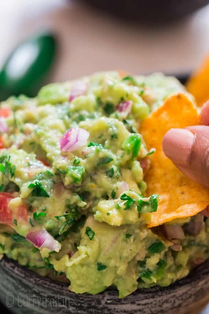 homemade guacamole with nachos scooping the dip