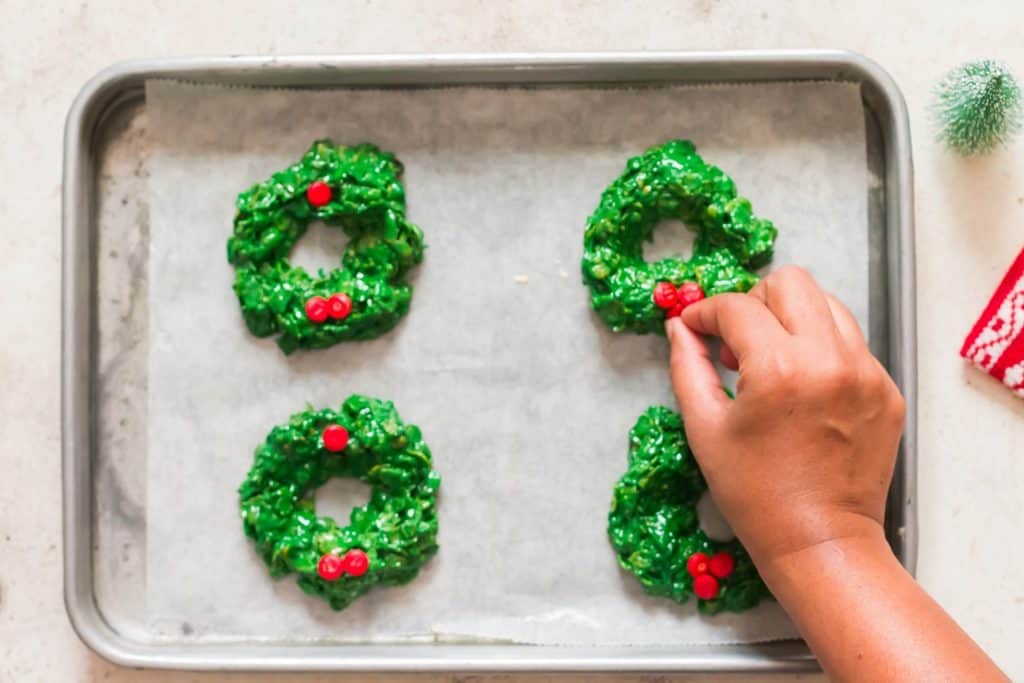 decorating Christmas wreath cookies with red candies