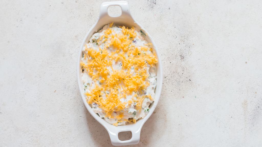 cheddar cheese sprinkled over cream cheese dip in a casserole dish.