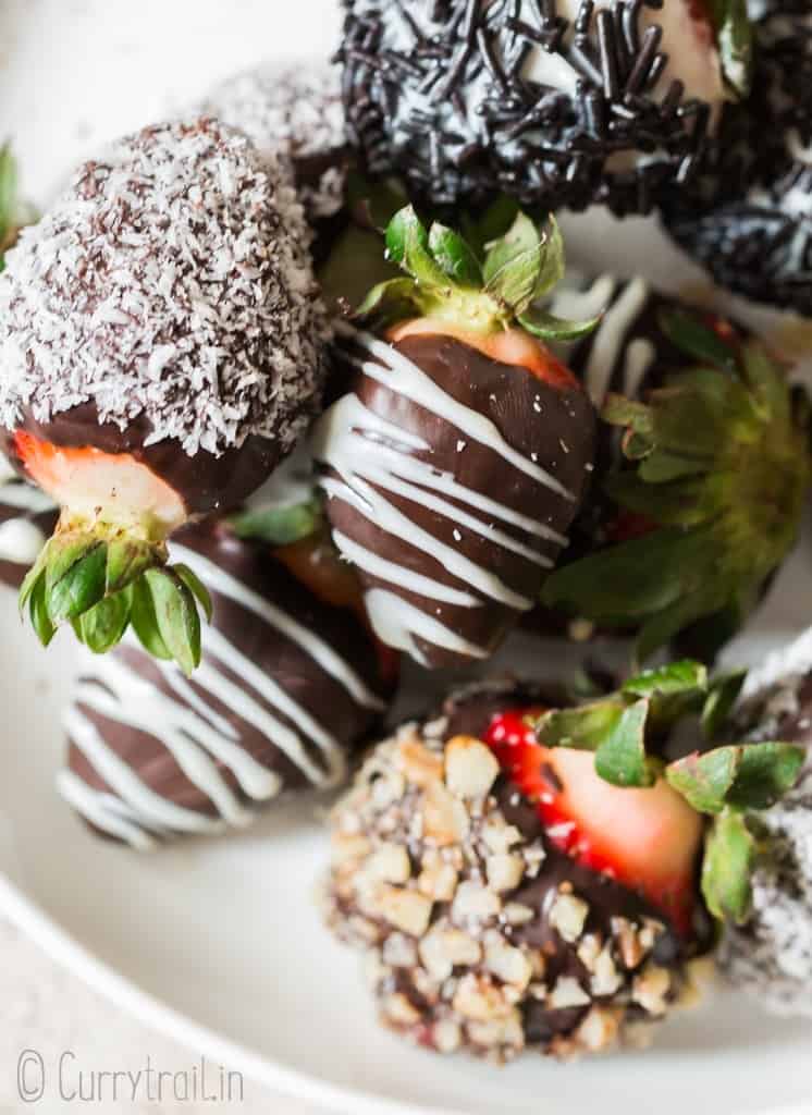 chocolate covered straberries decorated with chopped nuts, dessicated coconut and chocolate drizzle