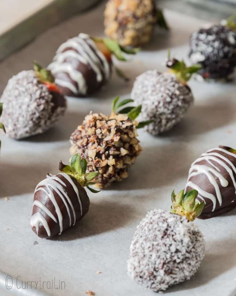 chocolate covered straberries decorated with chopped nuts, dessicated coconut and chocolate drizzle