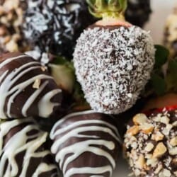chocolate covered straberries decorated with chopped nuts, dessicated coconut and chocolate drizzle