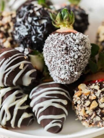 chocolate covered straberries decorated with chopped nuts, dessicated coconut and chocolate drizzle