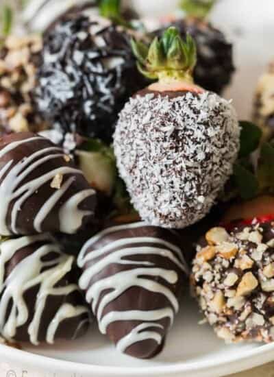 Chocolate-covered strawberries are decorated with chopped nuts, desiccated coconut, and chocolate drizzle.