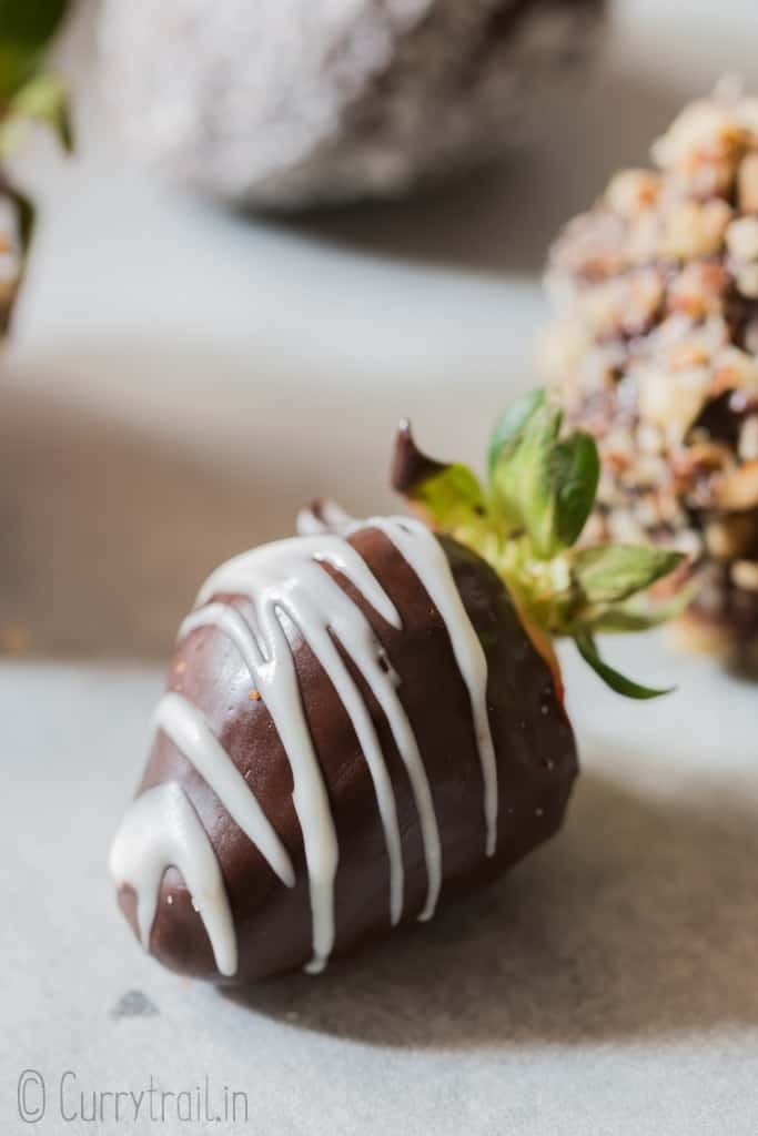 chocolate covered straberries decorated with chopped nuts, dessicated coconut and chocolate drizzle