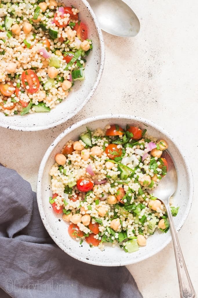 Isreali couscous salad in white bowl with spoon