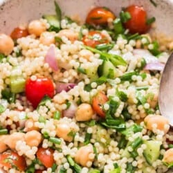 Isreali couscous salad in white bowl with spoon