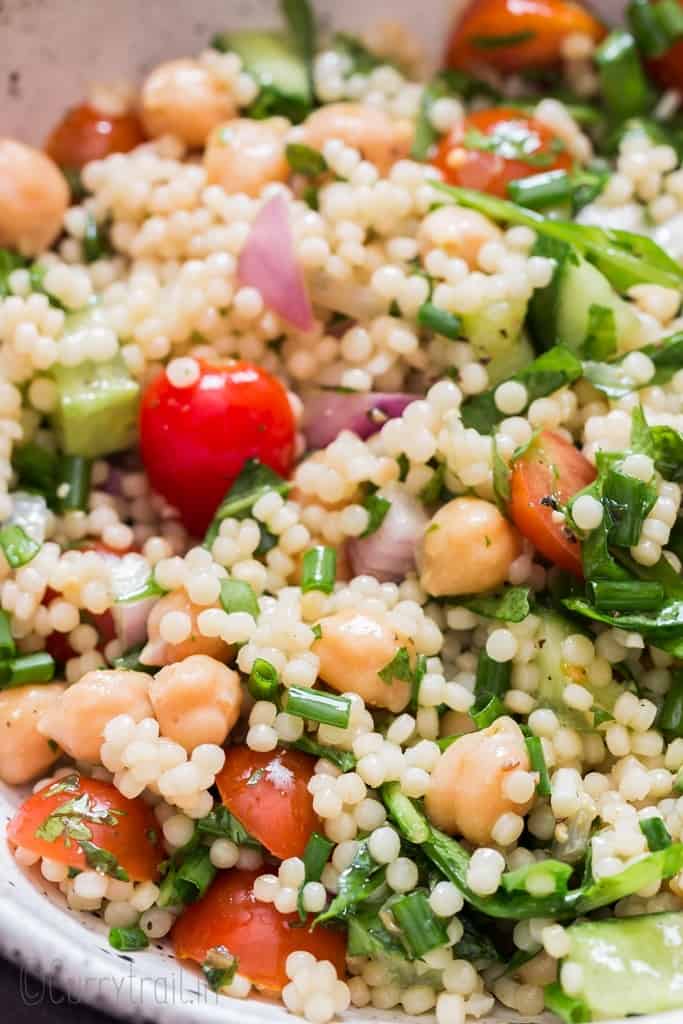 Isreali couscous salad in white bowl with spoon