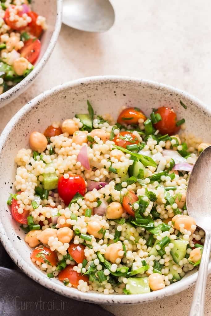 couscous salad served in two white bowls with spoons on the sides