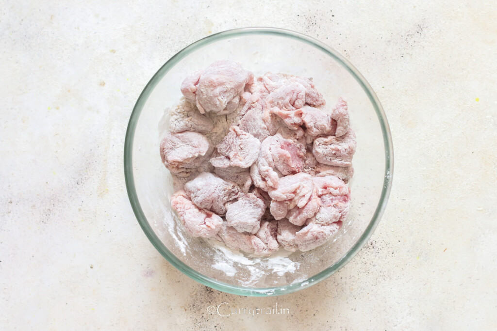 lamb pieces coated in flour, salt, and pepper in a bowl.