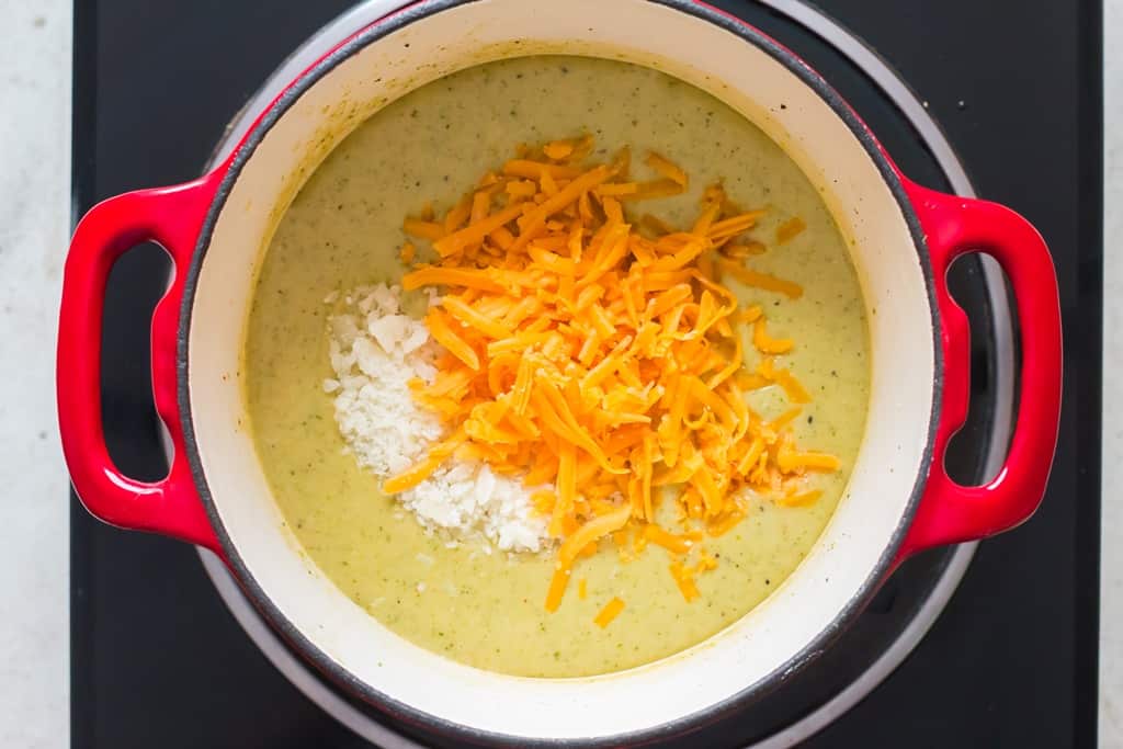 Parmesan cheese and grated cheddar cheese added to pot of hot broccoli and cheddar soup