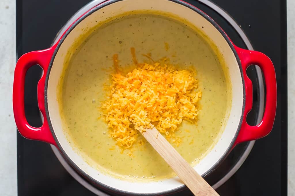 Parmesan cheese and grated cheddar cheese added to pot of hot broccoli and cheddar soup
