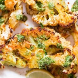 oven roasted cauliflower steaks served with chimichurri sauce on white plate