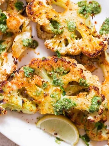 oven roasted cauliflower steaks served with chimichurri sauce on white plate