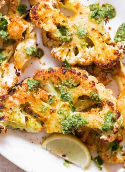 oven roasted cauliflower steaks served with chimichurri sauce on white plate