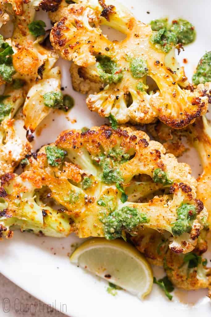 oven roasted cauliflower steaks served with chimichurri sauce on white plate