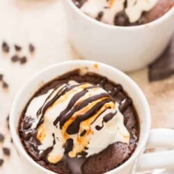 chocolate mug cake cooked in white mug topped with vanilla ice cream and chocolate caramel syrup