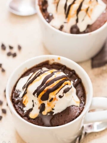 chocolate mug cake cooked in white mug topped with vanilla ice cream and chocolate caramel syrup