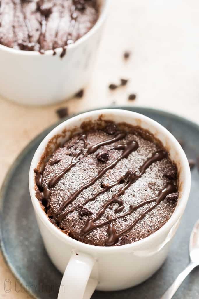 chocolate mug cake with powdered sugar and chocolate syrup drizzle on top
