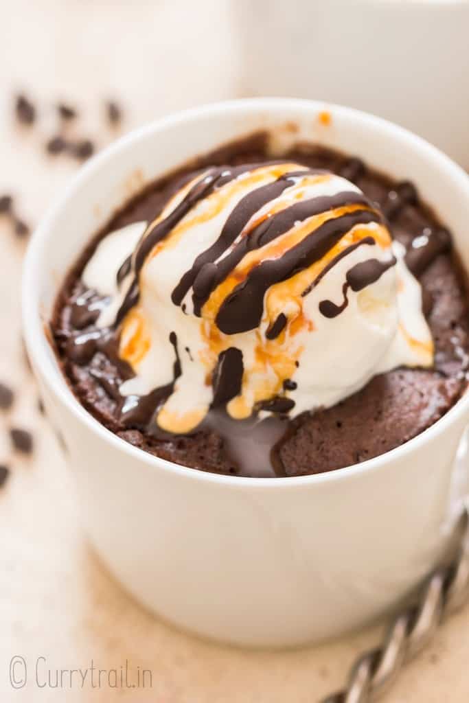 chocolate mug cake cooked in white mug topped with vanilla ice cream and chocolate caramel syrup