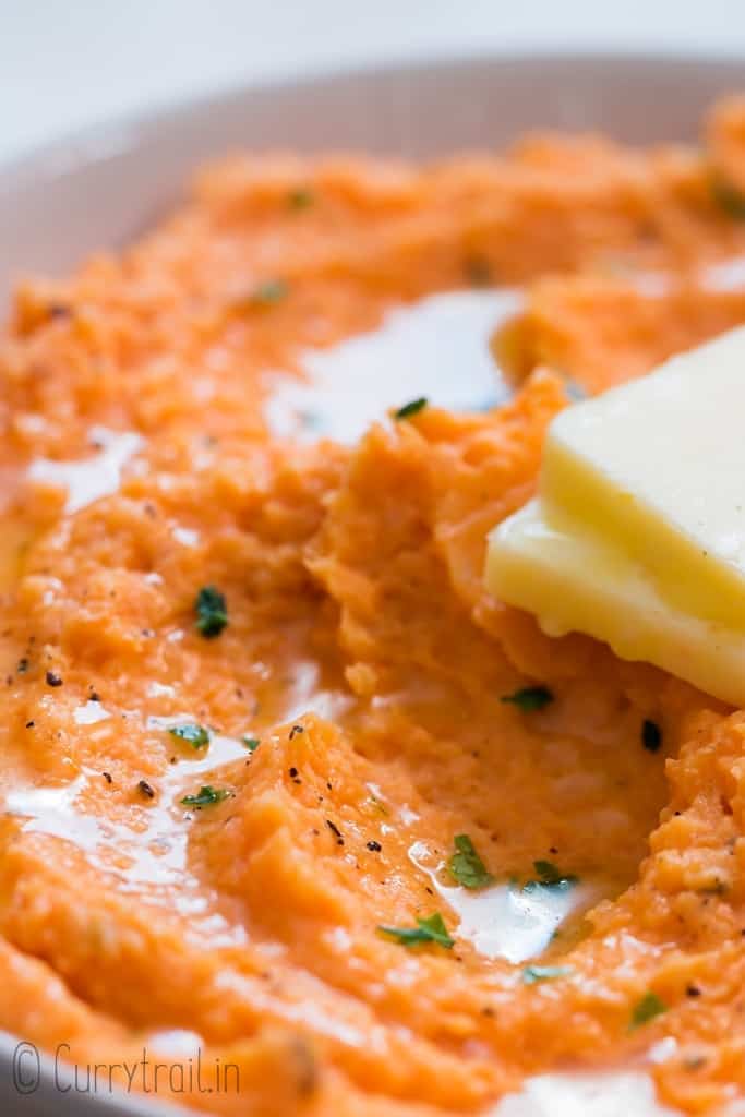 close up of mashed sweet potatoes served with cubed butter in white bowl