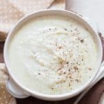 cheesy cauliflower cheese sauce served in while bowl with napkin on side