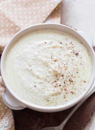 cheesy cauliflower cheese sauce served in while bowl with napkin on side