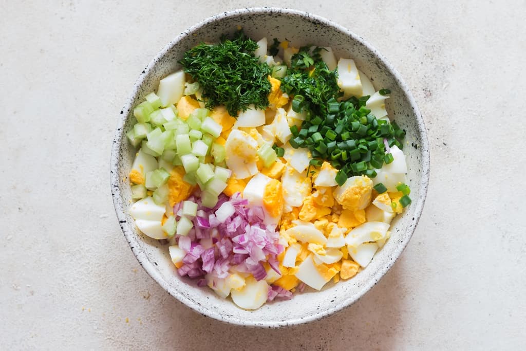 making egg salad in white bowl