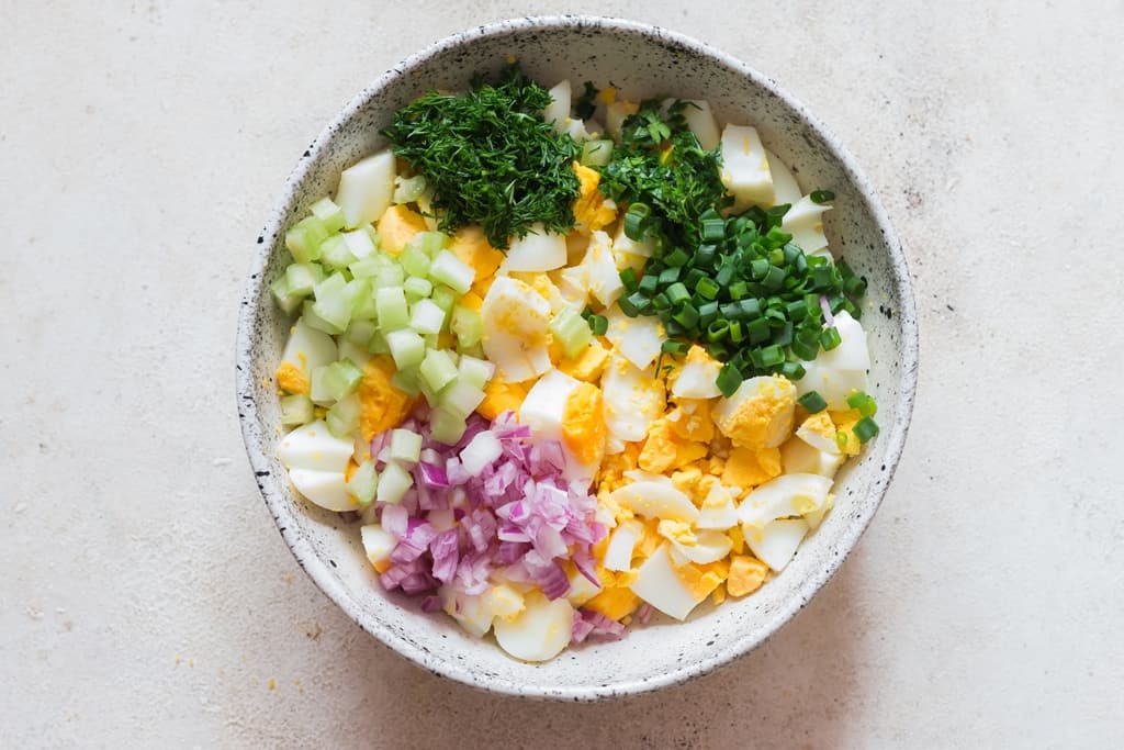 hard-boiled eggs with onion, celery, and fresh herbs in a bowl.