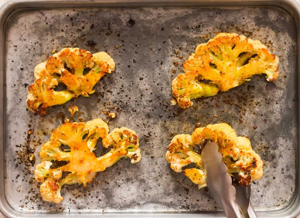 flipping roasted cauliflower steaks on baking tray