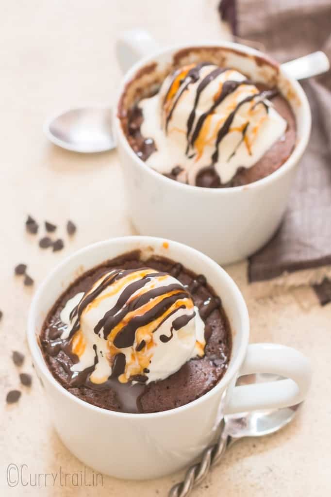 chocolate mug cake cooked in a white mug topped with vanilla ice cream and chocolate caramel syrup.