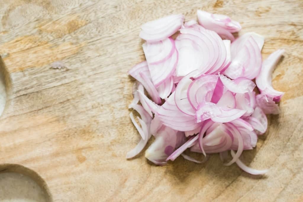 thinly sliced red onions on a wooden cutting board.