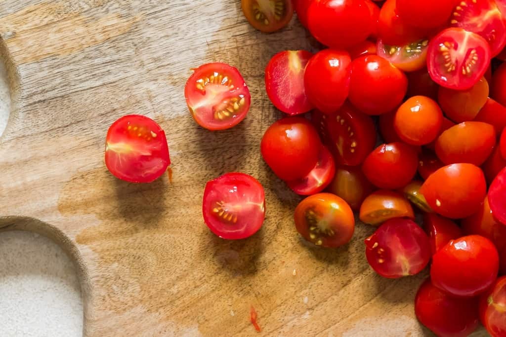 chopping tomatoes into halves on a wooden cutting board.