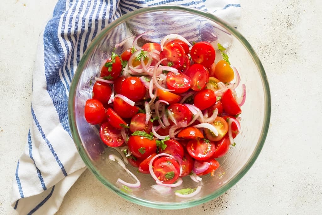 cherry tomato salad in a salad mixing bowl with a napkin on the side.