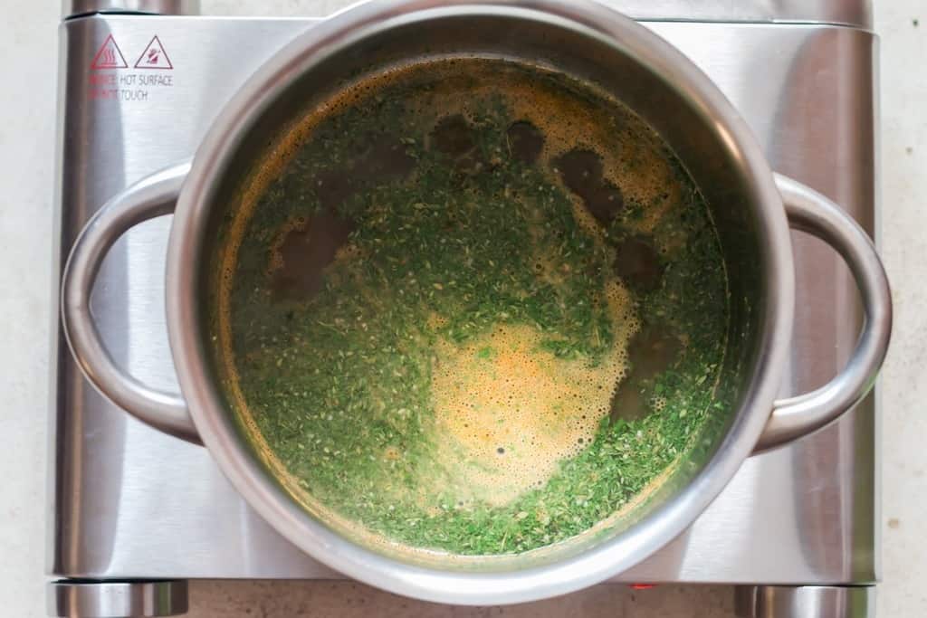 cooking rice, spices, and herbs in stock in the cooking pot.