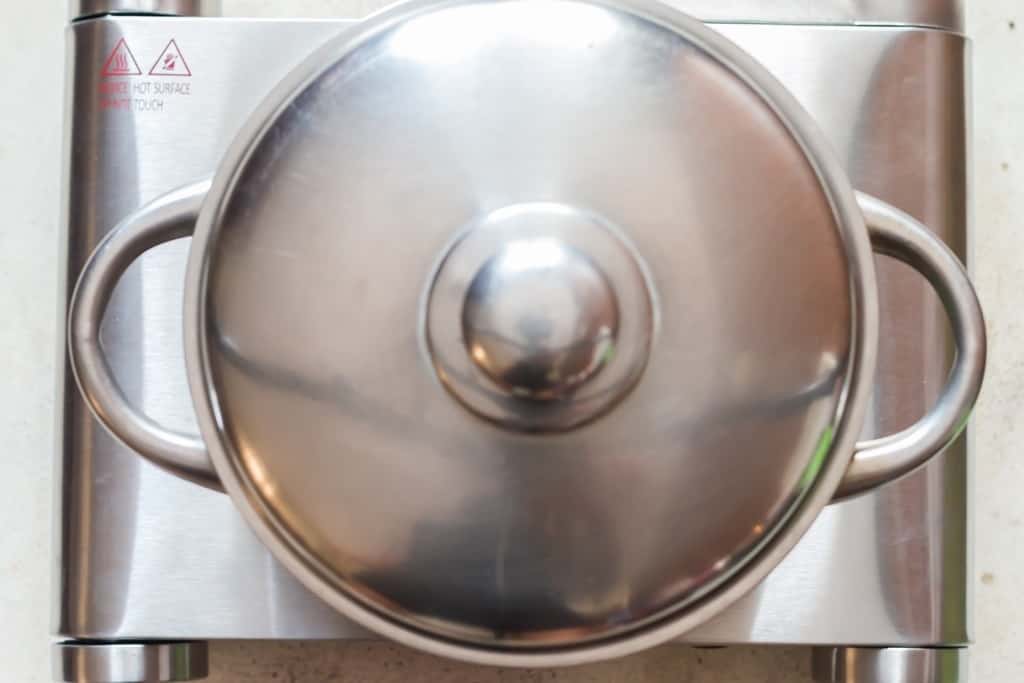 cooking rice with seasoning within a pot with a lid.