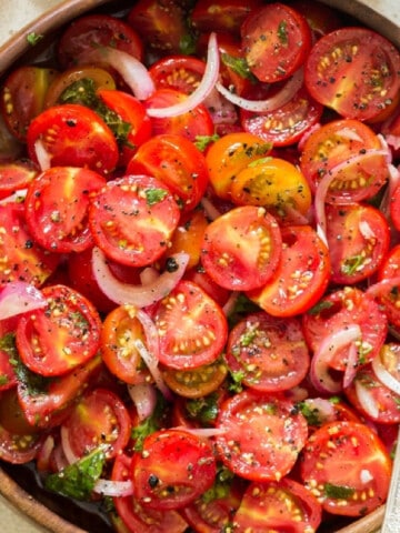 cherry tomato salad in a wooden salad bowl with a spoon in it.