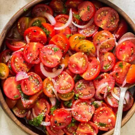 cherry tomato salad in a wooden salad bowl with a spoon in it.