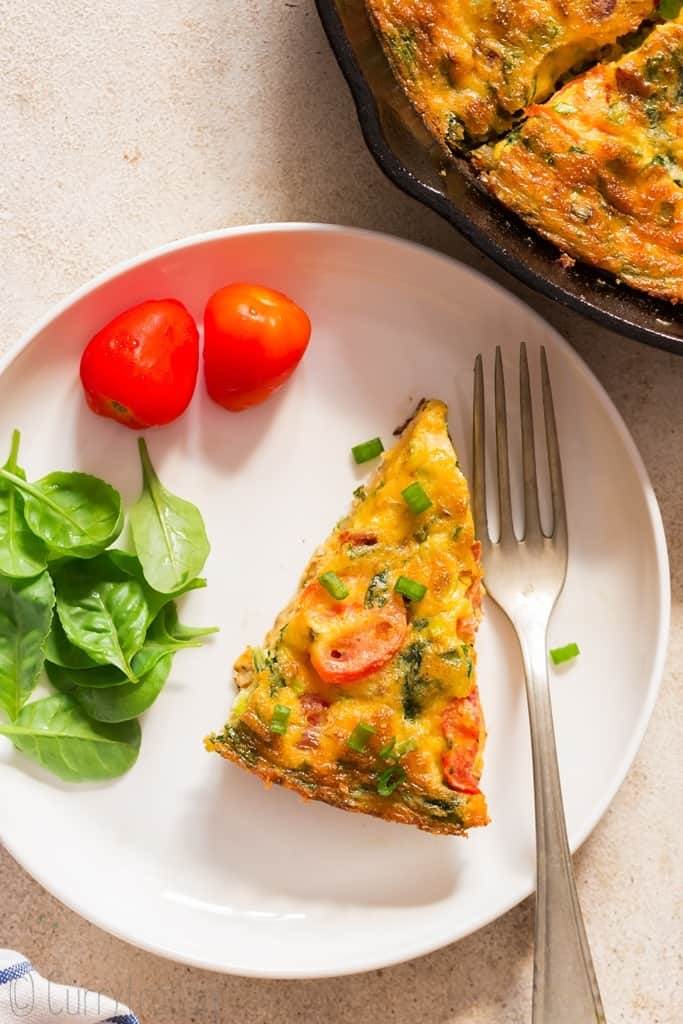 a slice of egg frittata on white plate with salad on side