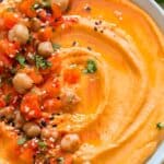 creamy roasted red pepper hummus made from scratch served in ceramic bowl with veggies and chips on sides