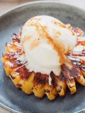 caramelized pineapple slice topped with vanilla ice cream on a blue plate.