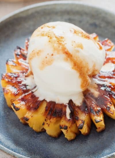 caramelized pineapple slice topped with vanilla ice cream on a blue plate.