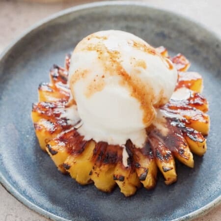 caramelized pineapple slice topped with vanilla ice cream on a blue plate.