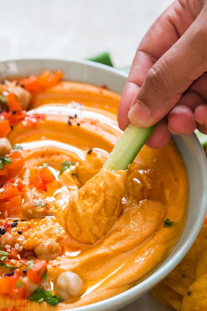 creamy roasted red pepper hummus made from scratch served in ceramic bowl with veggies and chips on sides