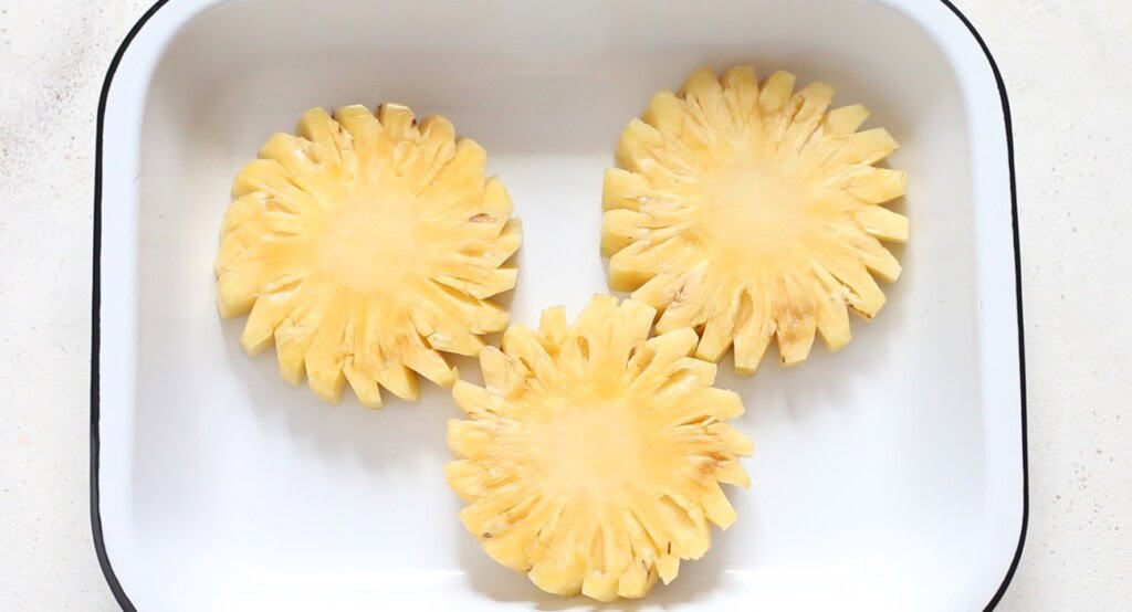 thick pineapple slices are placed in a white casserole.
