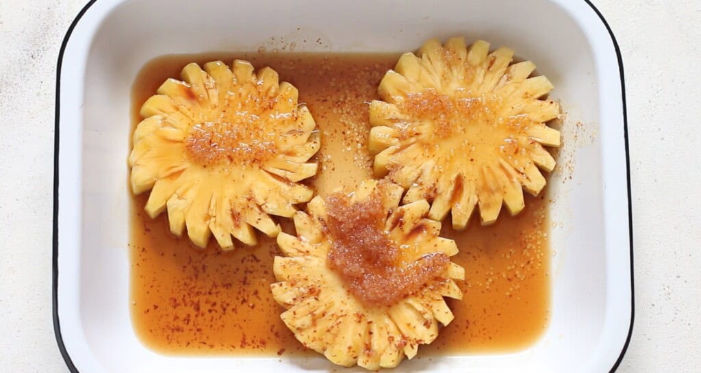 thick pineapple slices soaked in brown sugar and rum in a white casserole.