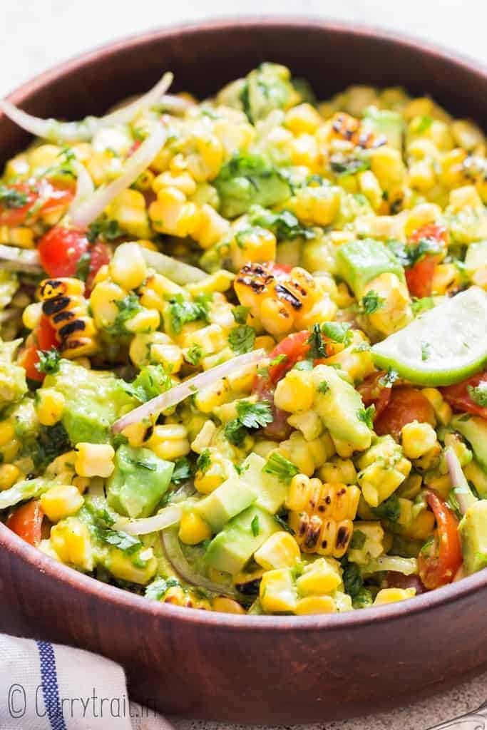 corn salad with avocados and cherry tomatoes in wooden bowl